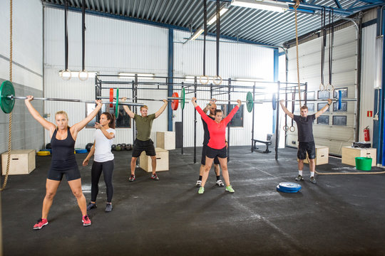 Instructor Assisting Athletes In Lifting Barbells