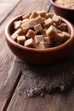 Brown sugar cubes and crystal sugar in bowl on wooden