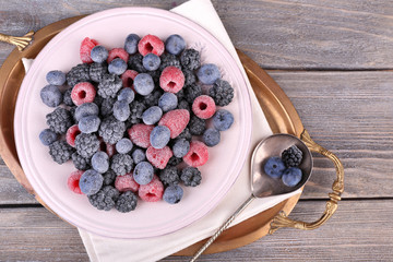 Iced berries on plate, on color wooden background