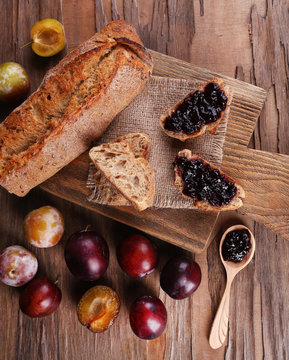 Bread with plum jam and plums on wooden table close-up
