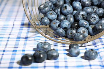 Tasty ripe blueberries in metal basket, on tablecloth