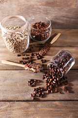 Glass jars and spoon with coffee beans on wooden background