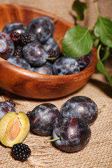 Ripe sweet plums in bowl, on wooden table