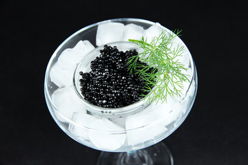 Glass bowl of black caviar and ice in goblet on dark background