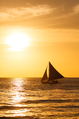 Fototapeta na wymiar Sailboat at sunset on a tropical sea. Silhouette photo.