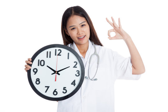 Young Asian female doctor show OK with a clock