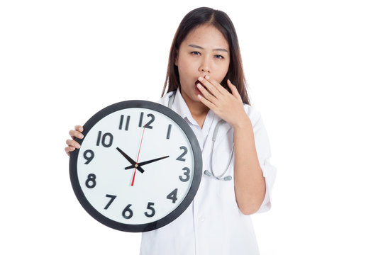 Young Asian female doctor yawn with a clock