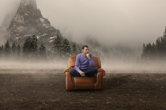 Crisis. Man in armchair in a foggy field with mountains behind