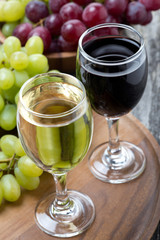 glasses of white and red wine, fresh grapes on wooden board