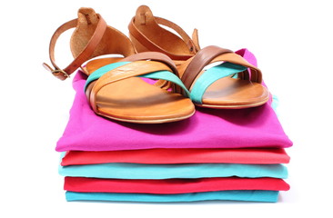 Woman sandals on pile of colorful clothes. White background