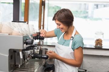 Pretty barista steaming jug of milk at coffee machine