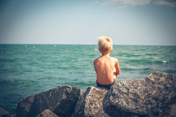Cute boy sitting on the stone in sea