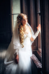 Obraz premium Beautiful bride in white wedding dress standing near the window