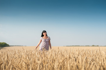Naklejka na ściany i meble Beautiful young woman walking on a field of wheat