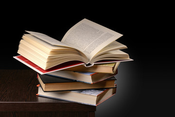 A pile of books with one of them open on the top, on the desk of a student at evening