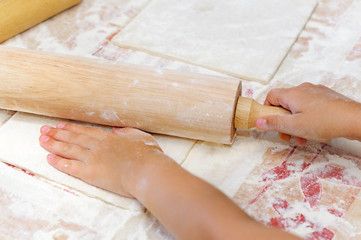 child unrolls dough with rolling pin