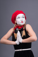 Portrait of female mime with red hat and white face grimacing wi