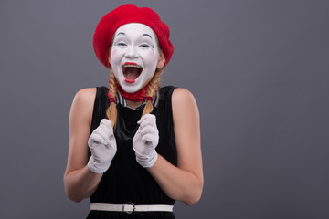 Portrait of female mime with red hat and white face grimacing wi