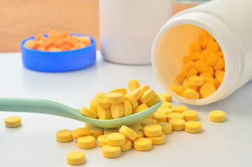 yellow medicine tablet on the spoon and open bottle of medicine