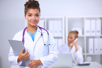 Fototapeta premium Smiling female doctor with a folder in uniform standing at hosp