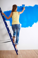 Happy beautiful young woman doing wall painting, standing on la