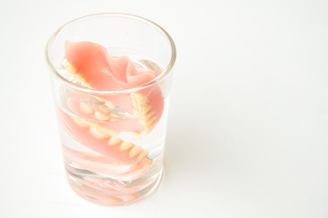 An artificial denture in a glass of water on isolated background