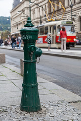 Fototapeta na wymiar antiker Hydrant mit einer Prager Straßenszene im Hintergrund