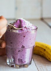 eating blueberry banana smoothie with coconut in a glass