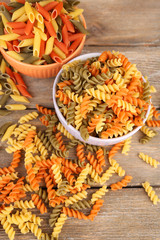 Assortment of colorful pasta in color bowls on wooden