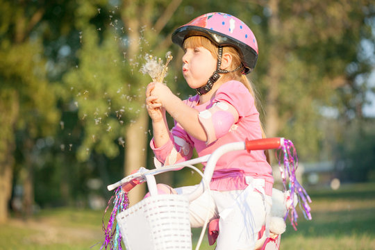  blond little girl on her bike blowing a dandelion