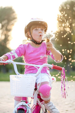  blond little girl on her bike blowing a dandelion