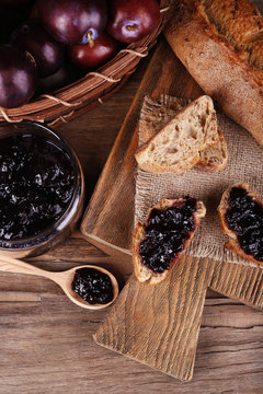 Bread with plum jam and plums on wooden table close-up