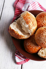 Tasty buns with sesame on plate, on color wooden background
