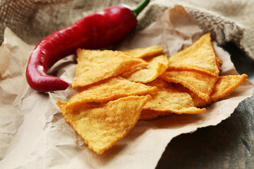 Tasty nachos and chili pepper on paper, on wooden background