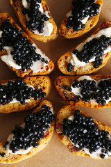 Slices of bread with butter and black caviar on paper