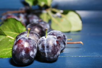 Ripe sweet plums with leaves, on wooden table