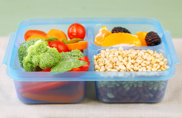 Tasty vegetarian food in plastic box on green wooden table