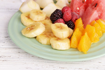 Sliced fruits and berries on plate on wooden table