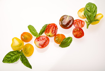 Sliced cherry tomatoes and basil leaves on white background