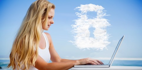 Composite image of pretty blonde using her laptop at the beach
