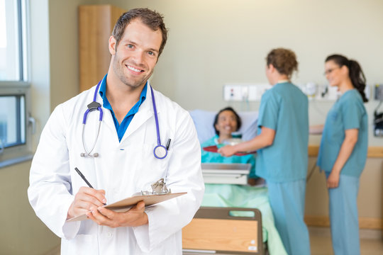 Confident Doctor Holding Clipboard While Nurses Serving Breakfas