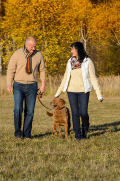 Couple walking dog in autumn sunny park