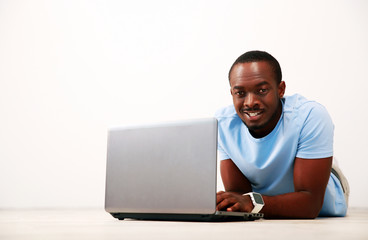 Portrait of a happy african man lying on the floor with laptop