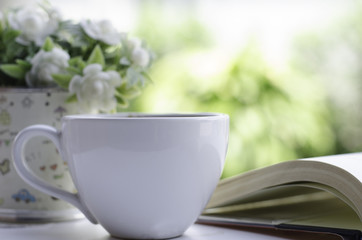 white cup of hot coffee with open book in the garden