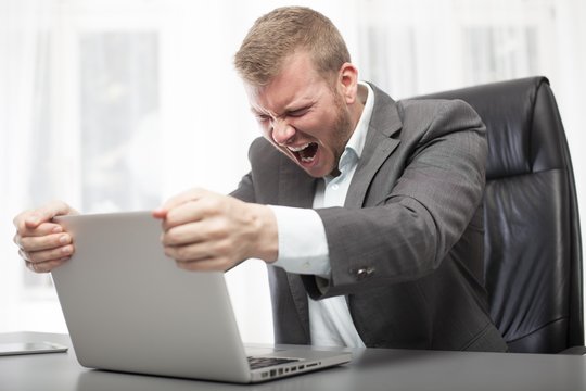 Angry businessman shaking his laptop computer