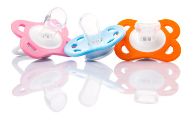 Orange, pink and blue pacifier over white background 