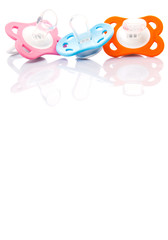 Orange, pink and blue pacifier over white background 