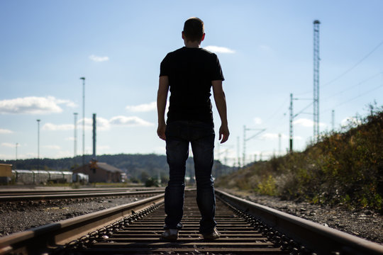Silhouette of a man from behind standing on railway tracks