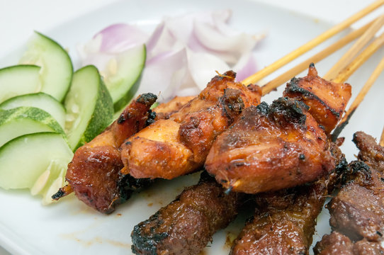 Delicious satay with cucumbers and onions served on white plate