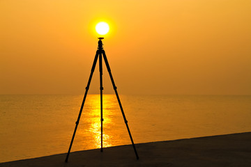 Tripod with the sun setting  on the tripod beside the sea